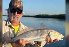 Angler in a camo cap and sunglasses holding a redfish
