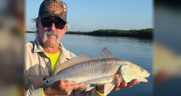 Angler in a camo cap and sunglasses holding a redfish