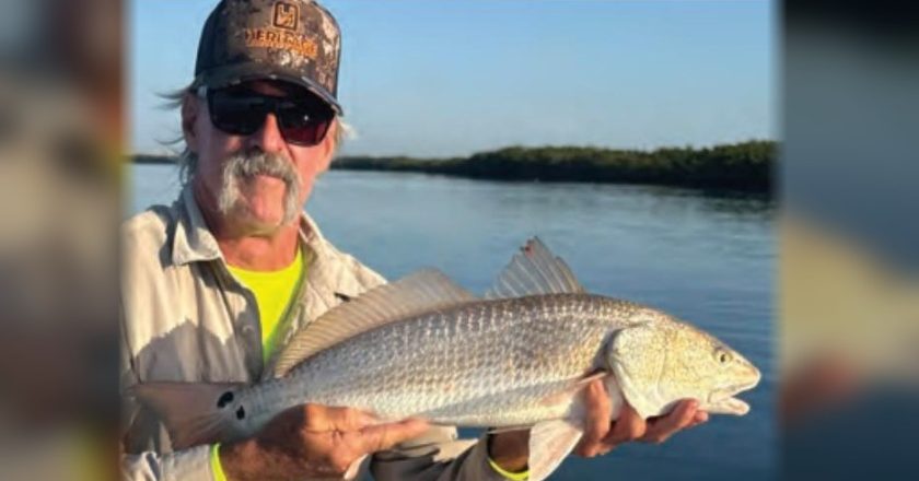 Angler in a camo cap and sunglasses holding a redfish