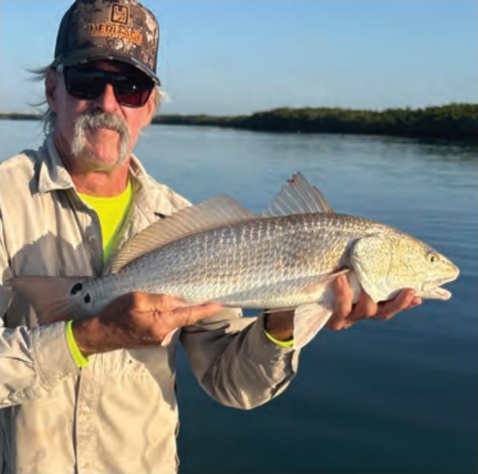 Angler in a camo cap and sunglasses holding a redfish