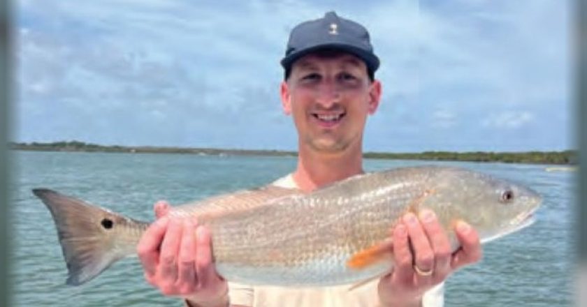 Smiling angler holding a redfish on a boat
