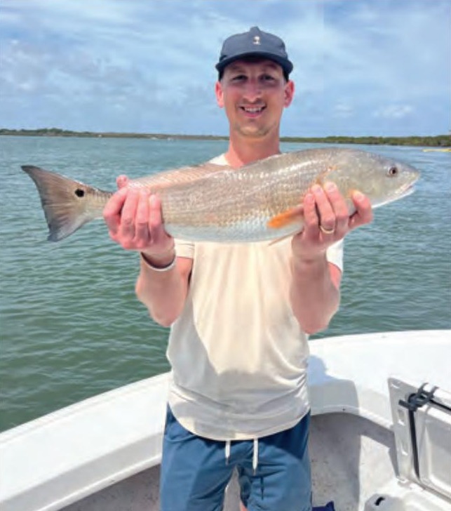 Smiling angler holding a redfish on a boat