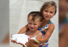 Two young children holding a pompano on the beach
