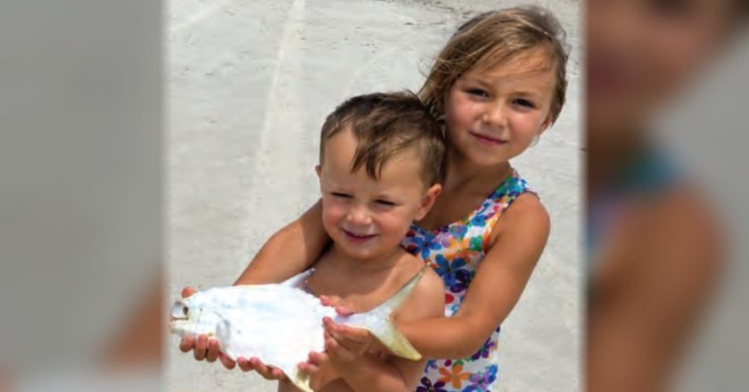 Two young children holding a pompano on the beach
