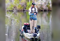 An angler standing on a fishing kayak on a tree-lined river