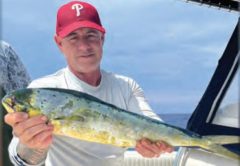 An angler in a red cap holding a mahi on a boat