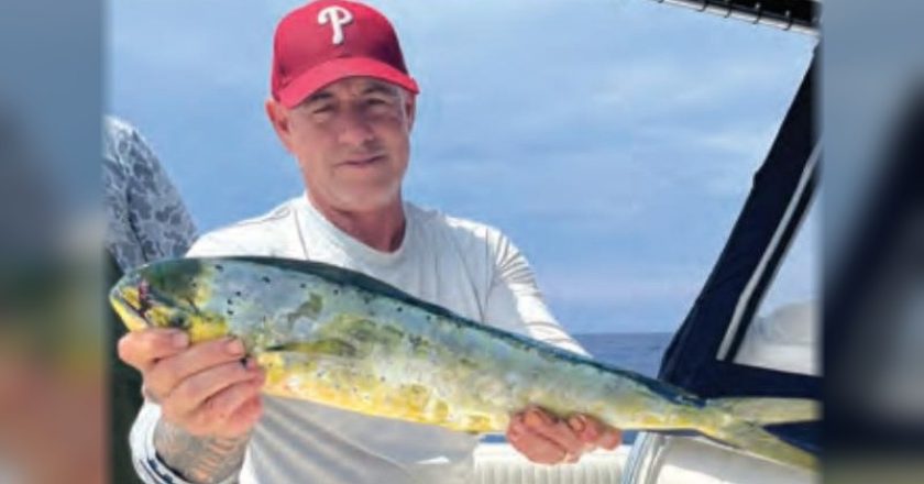 An angler in a red cap holding a mahi on a boat