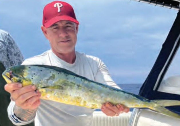 An angler in a red cap holding a mahi on a boat