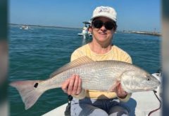 An angler in a white cap holding a redfish on the bow of a boat