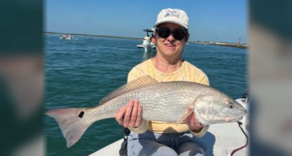 An angler in a white cap holding a redfish on the bow of a boat