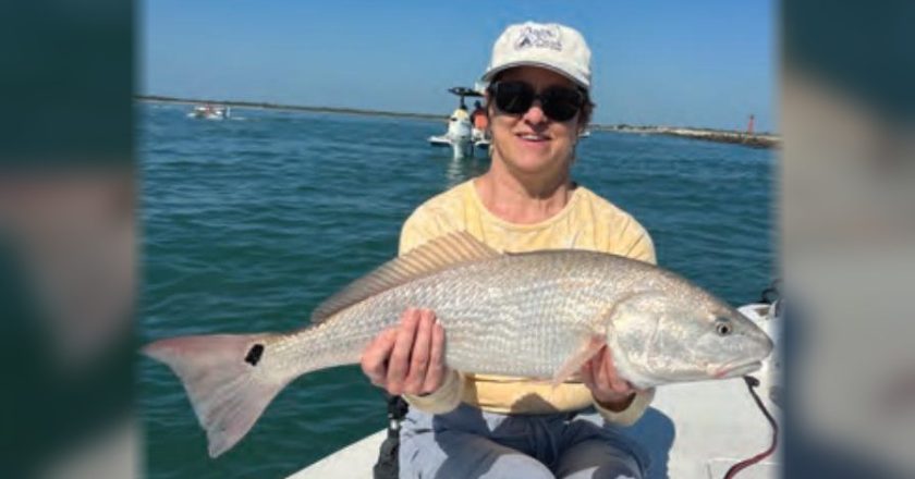 An angler in a white cap holding a redfish on the bow of a boat