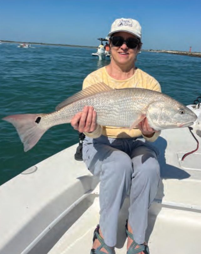 An angler in a white cap holding a redfish on the bow of a boat