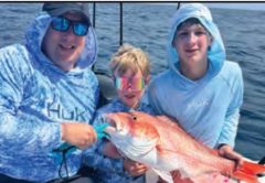 Two kids and an adult angler holding a red snapper offshore