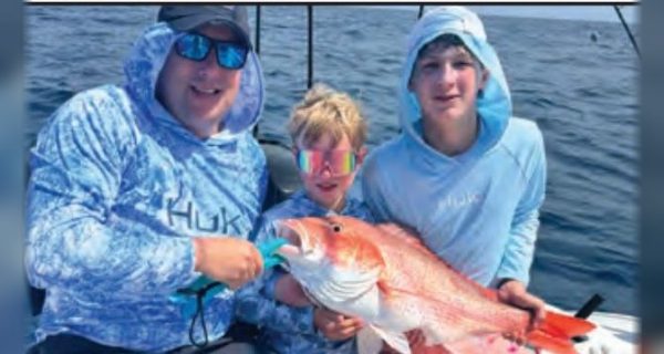 Two kids and an adult angler holding a red snapper offshore