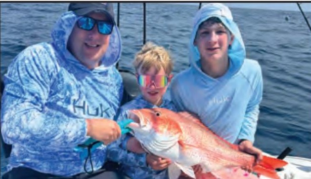Two kids and an adult angler holding a red snapper offshore