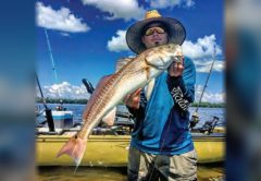 An angler in a straw hat holding a redfish