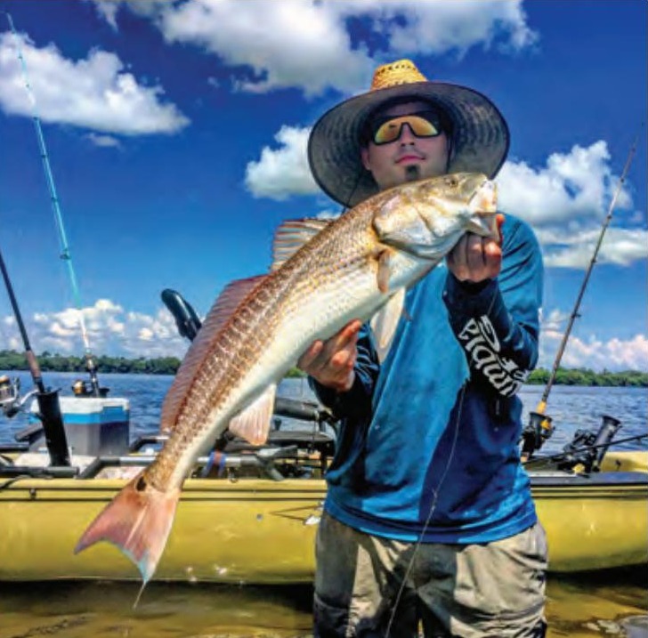 An angler in a straw hat holding a redfish