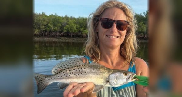 An angler holding a spotted seatrout in front of the mangroves