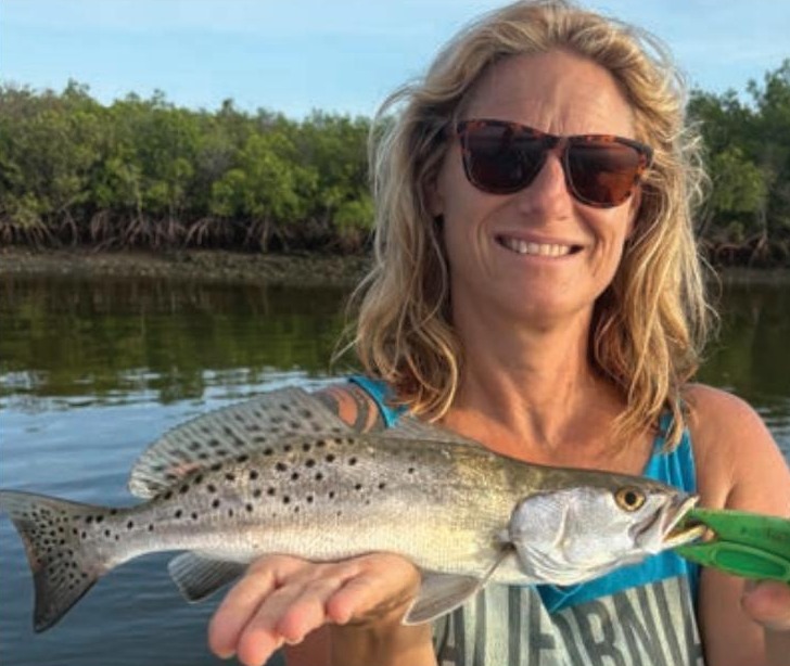 An angler holding a spotted seatrout in front of the mangroves