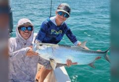 Two anglers holding a tarpon on the bow of a boat
