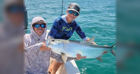 Two anglers holding a tarpon on the bow of a boat