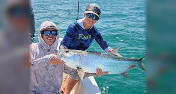 Two anglers holding a tarpon on the bow of a boat