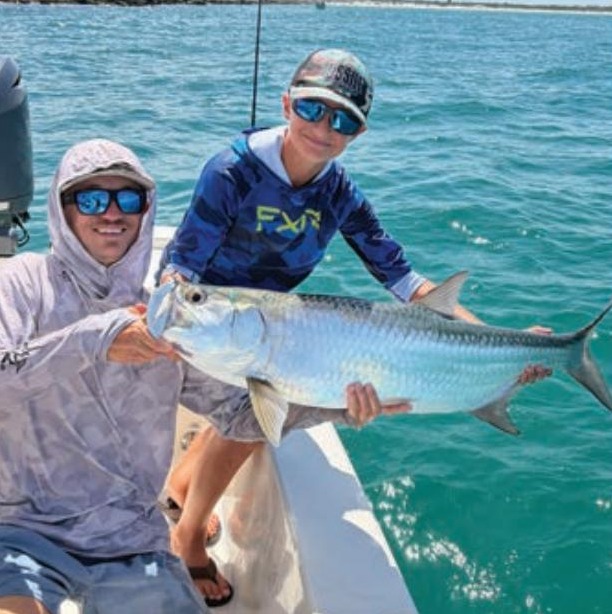 Two anglers holding a tarpon on the bow of a boat