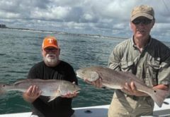 Two anglers holding bull redfish on a boat
