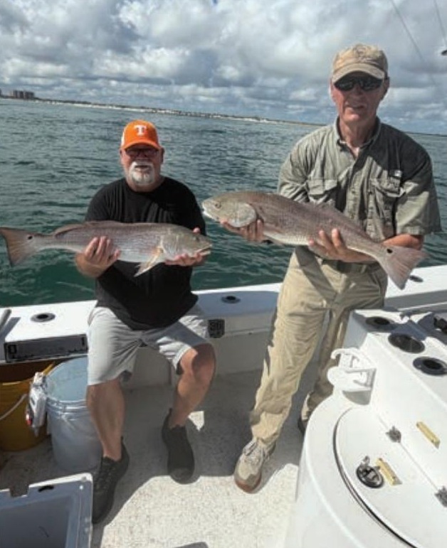 Two anglers holding bull redfish on a boat