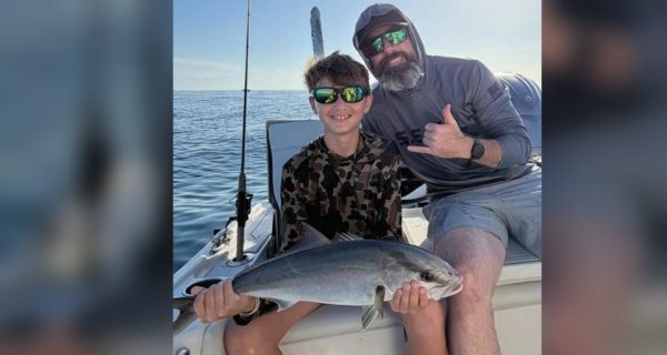 Youth angler holding an amberjack alongside Captain Evan Sanders of Sol Fishing