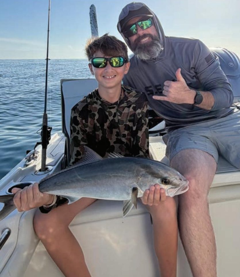 Youth angler holding an amberjack alongside Captain Evan Sanders of Sol Fishing